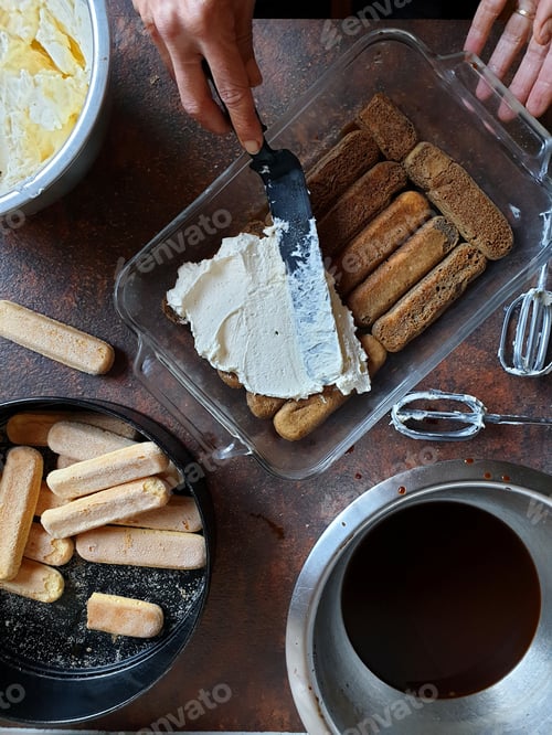 Preview: Person applying cream to sponge finger biscuit in glass dish for tiramisu cake