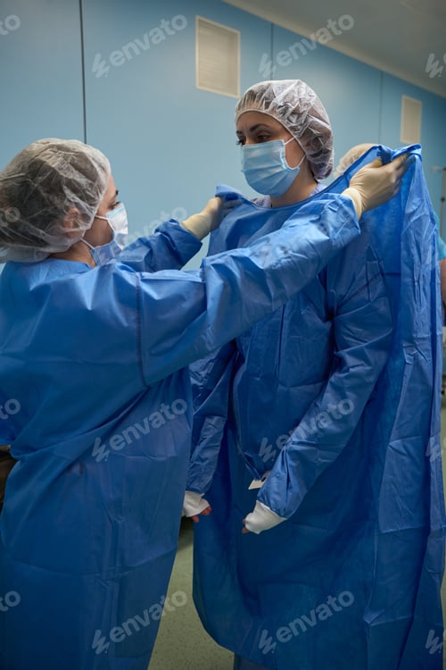 Preview: Nurse assisting doctor in wearing sterile gown in surgical theater