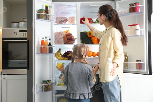 Preview: Young mother and her daughter with products near open refrigerator in kitchen