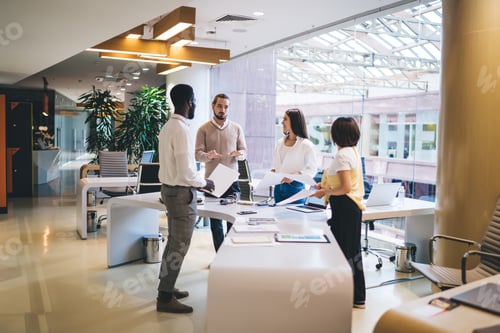 Preview: young multiracial partners standing near table desktop talking and analyzing financial documents