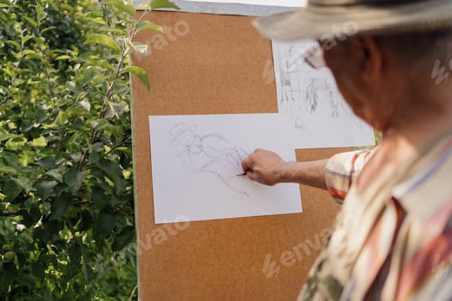 Preview: Senior man painting while relaxing in the garden among trees. Hobby and healthy lifestyle