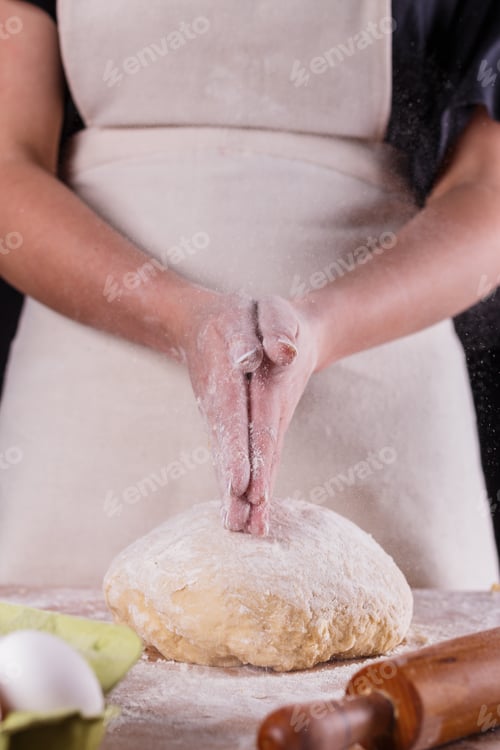 Preview: young woman in apron kneading dough on board
