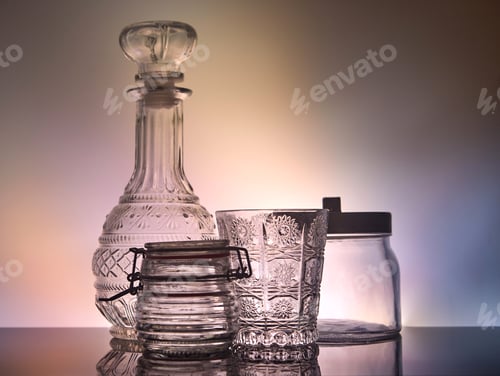 Preview: A decanter, a glass and glass jars standing on a stand with reflection with unusual lighting