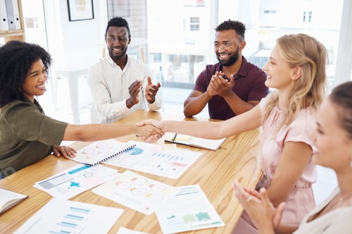 Preview: Female coworkers shaking hands while their colleagues clap hands. Group of diverse businesspeople h