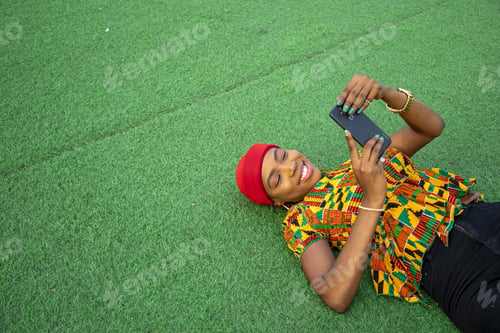 Preview: Beautiful young black female laying on the floor in a park using her mobile phone
