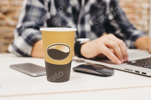 Preview: Young man using laptop at table with cup and smartphone