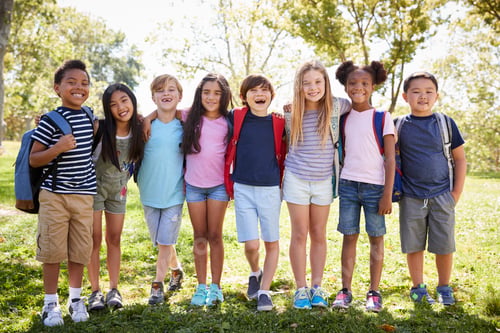 Preview: School kids stand embracing in a row outdoors, full length