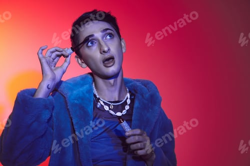 Preview: alluring androgynous man in purple stylish faux fur using mascara while on vibrant background