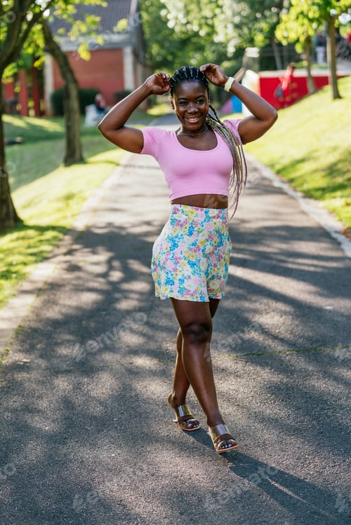 Preview: A woman in a pink shirt and floral shorts is walking down a street