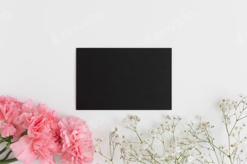 Preview: Top view of a black card mockup with gypsophila and a bouquet of pink carnations on a white table.