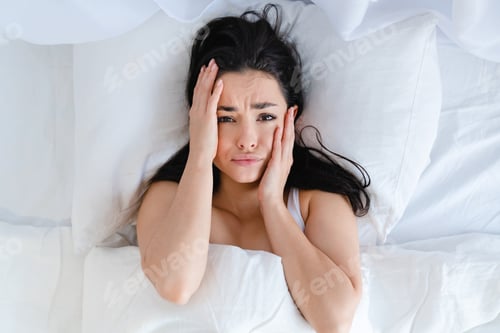 Preview: Sad young caucasian woman lying in the bed with white linen because of the insomnia
