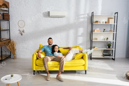 Preview: Handsome man smiling at camera near beautiful girlfriend lying on couch in living room