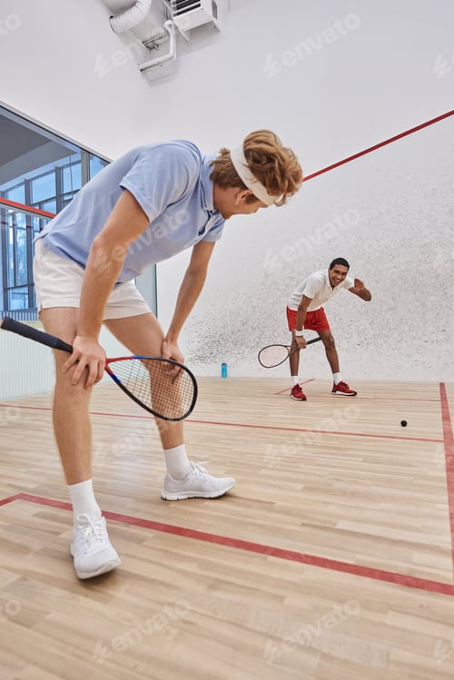 Preview: tired interracial players in sportswear breathing heavily after playing squash in court, motivation