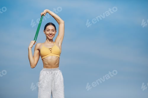 Preview: Woman Exercises Outdoors with Resistance Band Under Blue Sky