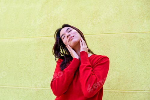 Preview: Young Asian woman with her eyes closed, hands touching her neck and jawline