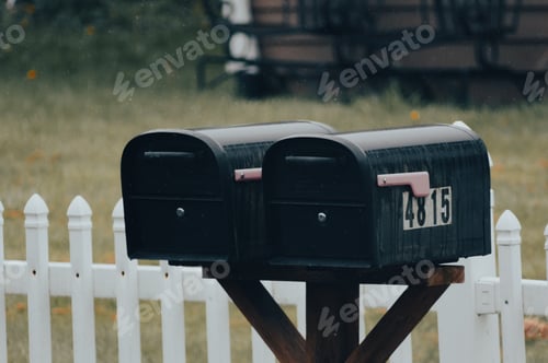 Preview: Close-up of mailboxes on a post in front of a white fence