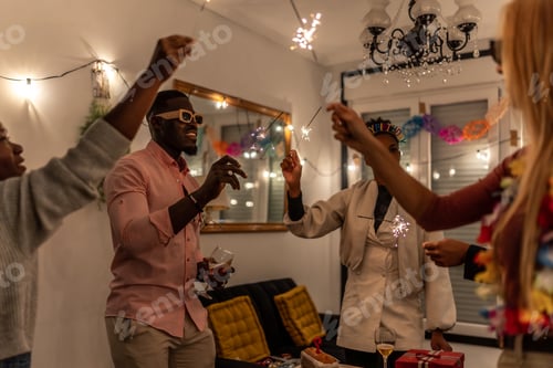 Preview: Happy multiracial friends dancing raising burning sparkles at home