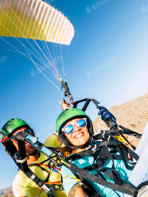 Preview: Active young adult people woman enjoy paraglide activity flying in the sky with professional pilote