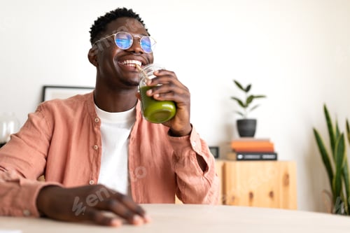 Preview: African American man drinks green juice with bamboo straw looking at camera. Copy space.