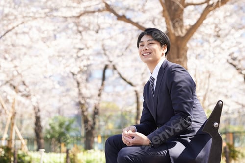 Preview: A Japanese male businessman sits on a park bench with a smile on his face