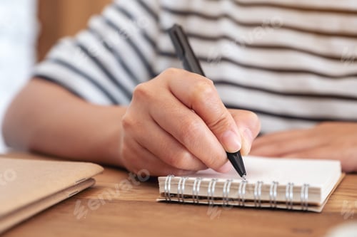 Preview: Closeup image of a woman's hand writing on blank notebook on wooden table