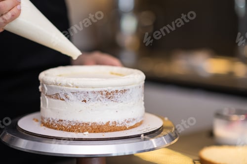 Preview: Professional confectioner smearing gluten free cake layers with white cream using pastry cone