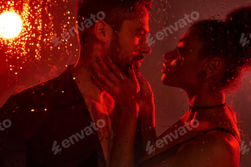 Preview: A passionate embrace captured in warm red light on a rainy night