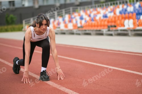 Preview: The athletic woman prepares to start a race on the track, her focused expression and stance