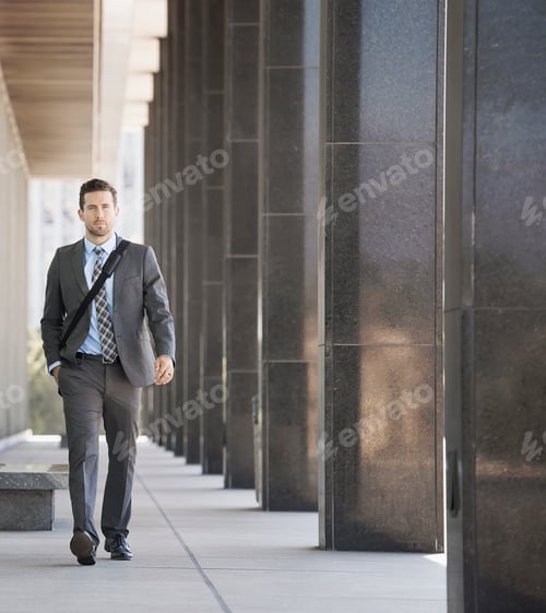 Preview: A businessman with a laptop bag walking along a city sidewalk.
