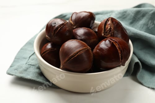 Preview: Roasted edible sweet chestnuts in bowl on white table, closeup