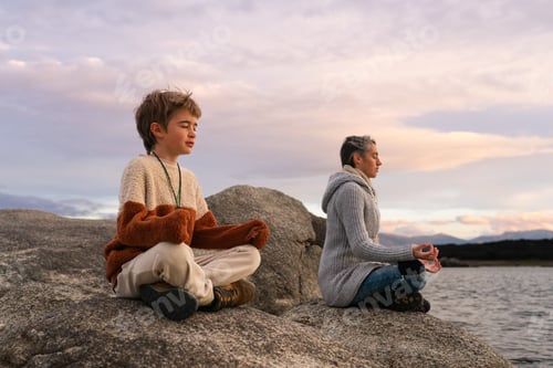 Preview: Family of mother and 9 year old son meditating at sunrise in nature with copy space