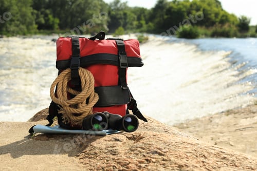 Preview: Backpack and camping equipment on stone near river. Space for text
