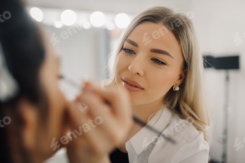 Preview: Makeup artist applying makeup on model's face in beauty salon