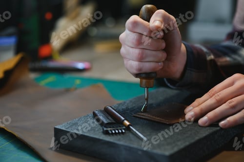 Preview: Production process. Young focused experienced master craftsman makes leather goods at his workplace