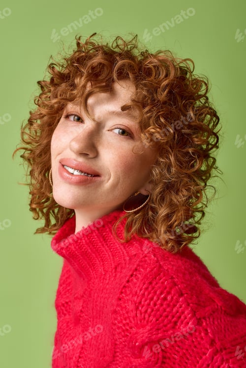 Preview: Young woman with red curls and sweater shines joyfully in a green setting