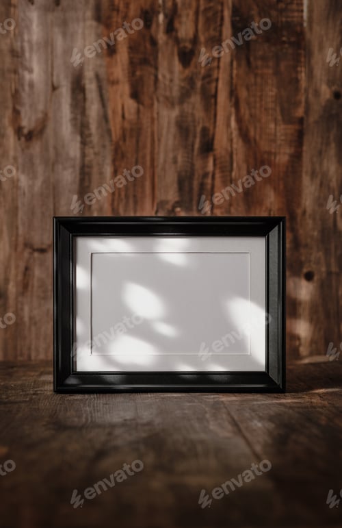 Preview: blank black photo frame on wood table and wall witn sunlight from window