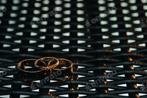 Preview: Two wedding rings and one engagement ring on a checkered grid. three gold rings of a couple in love