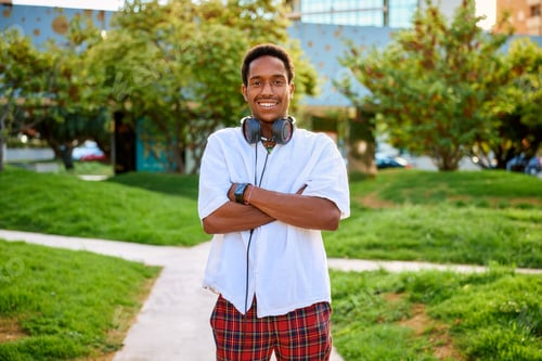 Preview: A young man smiles proudly with his arms crossed, wearing headphones, in a lively outdoor area