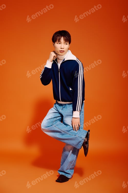 Preview: Stylish young man poses confidently against a vibrant orange backdrop showcasing modern fashion
