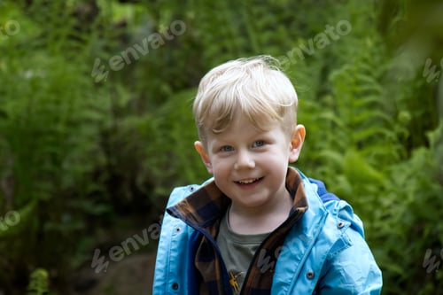 Preview: Portrait of a blond boy against a background of green foliage in the park copy space