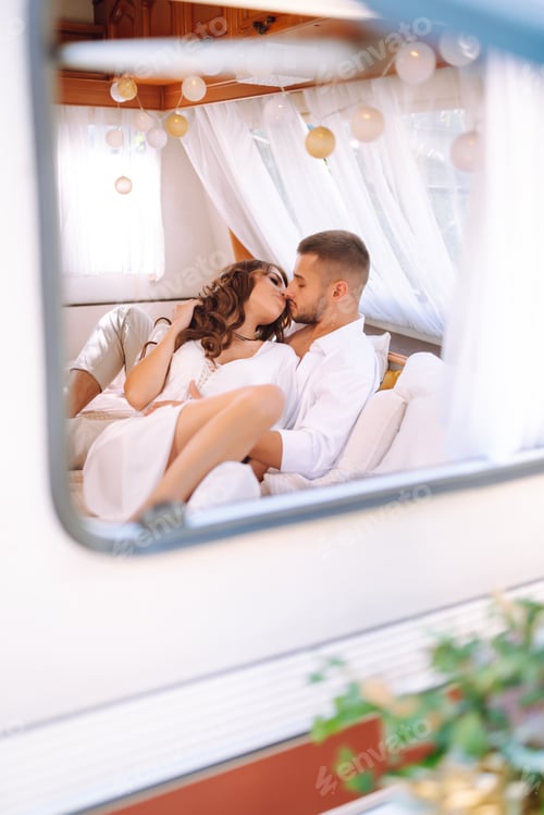 Preview: Happy newlyweds elaxing in rv, camping in a trailer. Couple embracing each other and smiling.