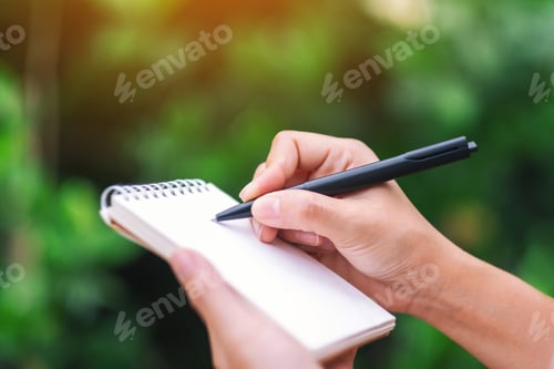 Preview: Closeup image of a woman's hands holding and writing on blank notebook in the outdoors