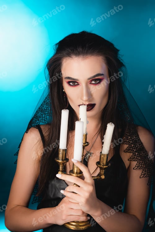 Preview: pale woman with black makeup holding burning candles on blue