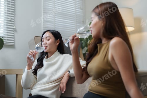 Preview: Two young women drinking water from wine glasses in living room