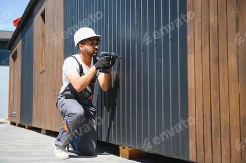 Preview: Construction worker using cordless drill installing modular house panel