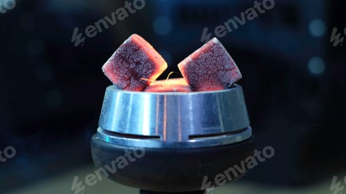 Preview: Close up of two hot charcoals with sparkles and smoke. Media. Hot red coals with hookah in bowl for