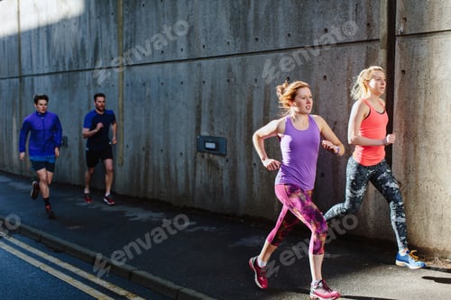 Preview: Four young adult runners running along city sidewalk