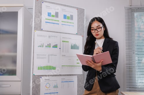 Preview: Businesswoman analyzing financial charts and taking notes in office meeting room