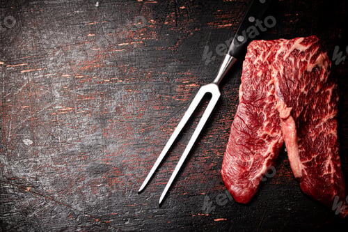 Preview: Raw steak with a large fork on the table.