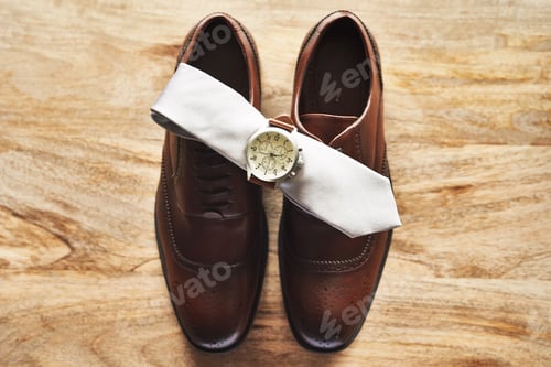 Preview: Still life shot of a wristwatch and tie on top of formal shoes on a wooden surface